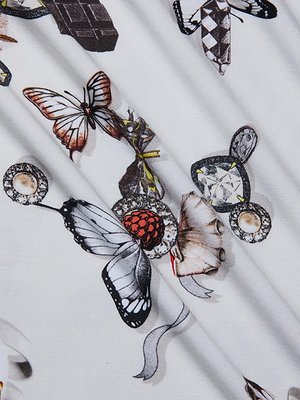 The Ressi Fitted Tee features patterned stretch jersey knit with butterflies, gemstones, pearls, and ribbons on a light background with subtle folds—perfect for a bestselling slim-cut top.