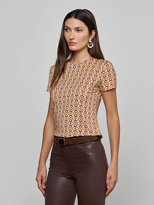 A woman with long brown hair wears the Ressi Fitted Tee in a graphic horse bit print, styled with dark brown pants, a black belt, and large gold hoop earrings, standing against a plain gray background.