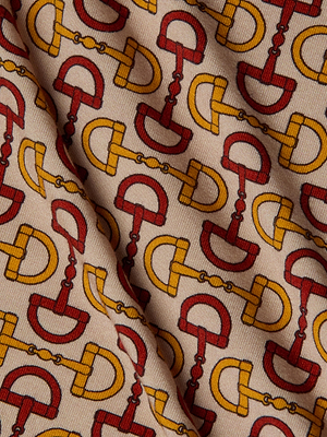 A close-up of stretch jersey knit on the Ressi Fitted Tee, showcasing a graphic horse bit print in red and yellow on beige, with subtle material folds. Ideal for a chic short sleeve look.