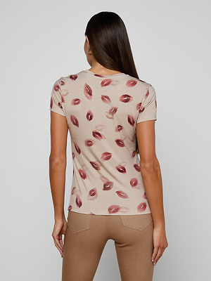 A woman with long brown hair wears the bestselling Ressi Fitted Tee in stretch jersey knit with a red lipstick kiss print and slim cut, paired with light brown pants, as she stands facing away against a plain background.