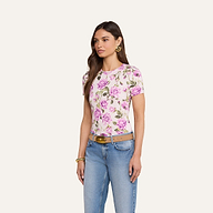 Una donna è in posa su uno sfondo beige e indossa la maglietta Ressi Fitted Tee, best seller in jersey elasticizzato con stampa di rose rosa, jeans blu, cintura color cuoio, orecchini dorati e un braccialetto dorato.