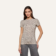 A woman is wearing the Ressi Fitted Tee, a short-sleeve beige and gray leopard print stretch jersey knit t-shirt, paired with gray pants. She stands against a plain, light-colored background facing forward with a neutral expression.