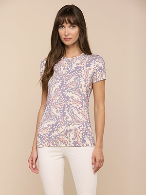 Eine Frau mit langen braunen Haaren trägt das meistverkaufte Ressi Fitted Tee mit pastellfarbenem Blumendruck aus Stretch-Jersey-Strick, gepaart mit einer weißen Hose vor einem neutralen beigen Hintergrund.