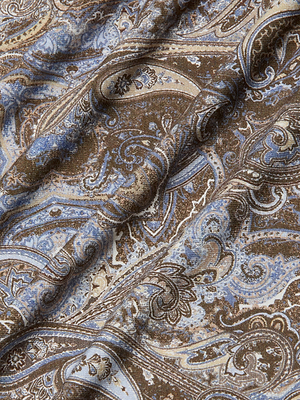 A close-up of brown fabric with an intricate paisley print in blue, beige, and cream adds texture to the Ressi Fitted Tee—perfect for a slim cut look or bestselling style.