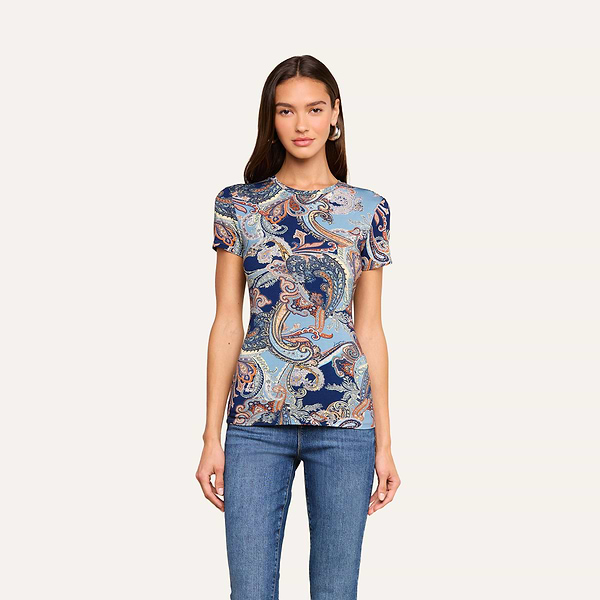 Vêtue dun t-shirt ajusté Ressi — un haut à manches courtes orné dun motif paisley bleu nuit —, une femme portant un jean bleu slim se tient de face devant un fond beige, lair impassible, les mains le long du corps.