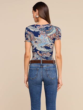 A woman is seen from behind wearing the Ressi Fitted Tee in a midnight blue paisley pattern, styled with blue jeans and a brown belt against a plain beige background.
