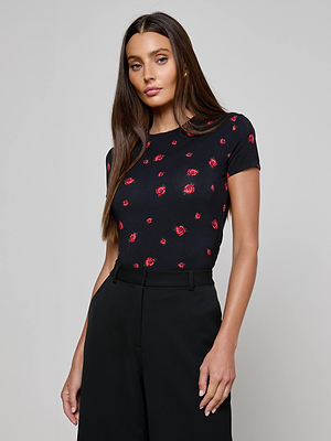 A woman with long brown hair wears a black Ressi Fitted Tee with a red rose print and black high-waisted pants, posing against a plain light gray background.
