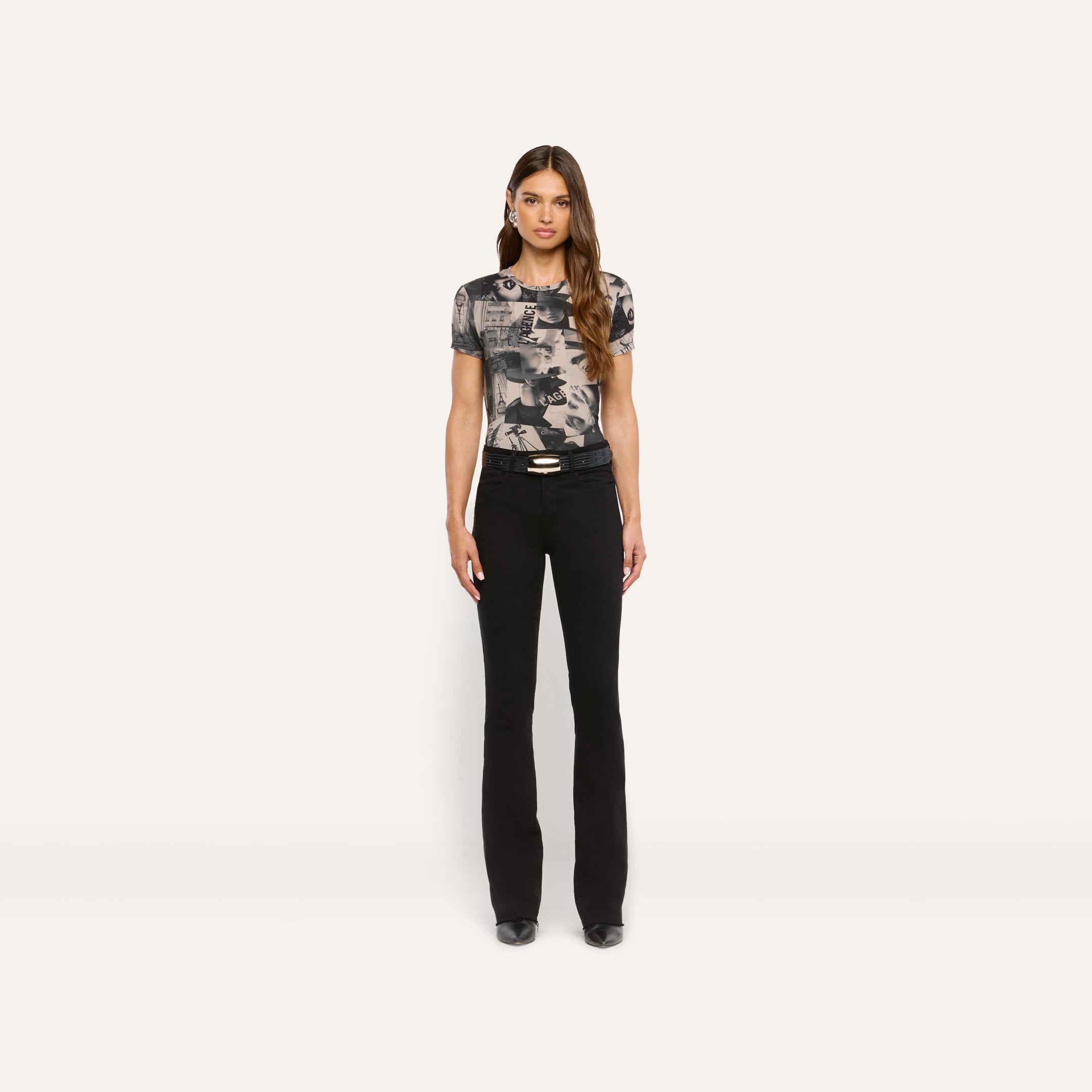 A person wearing a Ressi Fitted Tee featuring a black and white magazine collage print, paired with black flared jeans and a black belt.