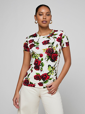A woman in hoop earrings models the Ressi Fitted Tee—a bestselling, white slim-cut t-shirt with a red rose print—paired with cream-colored pants, standing against a light gray background with one hand on her hip.