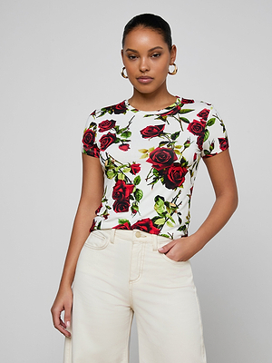 A woman stands with one hand in her cream pants pocket against a light gray background, wearing gold hoop earrings and the bestselling Ressi Fitted Tee featuring a red rose pattern.