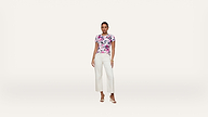 A woman stands against a white background, wearing a floral short-sleeve top, white wide-leg pants, and beige heeled sandals.