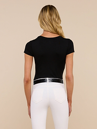 A woman with long blonde hair, wearing the Ressi Fitted Tee in black and white pants, stands facing away from the camera against a plain light background.