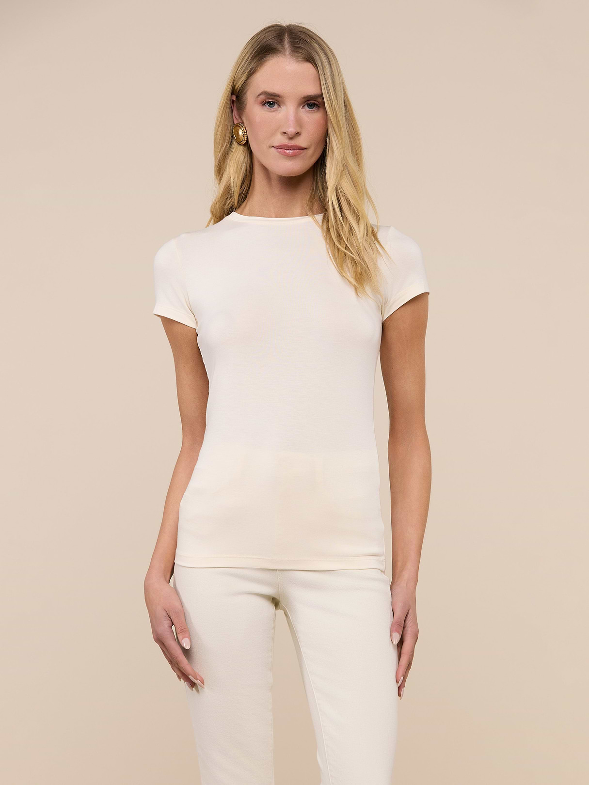 A woman with long blonde hair wears the Ressi Fitted Tee and matching pants in soft microfiber modal jersey, standing against a plain beige background, facing forward with a neutral expression.