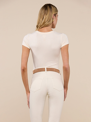 A woman with long blonde hair is shown from behind, wearing the Ressi Fitted Tee and high-waisted cream pants in soft microfiber modal jersey against a beige background.