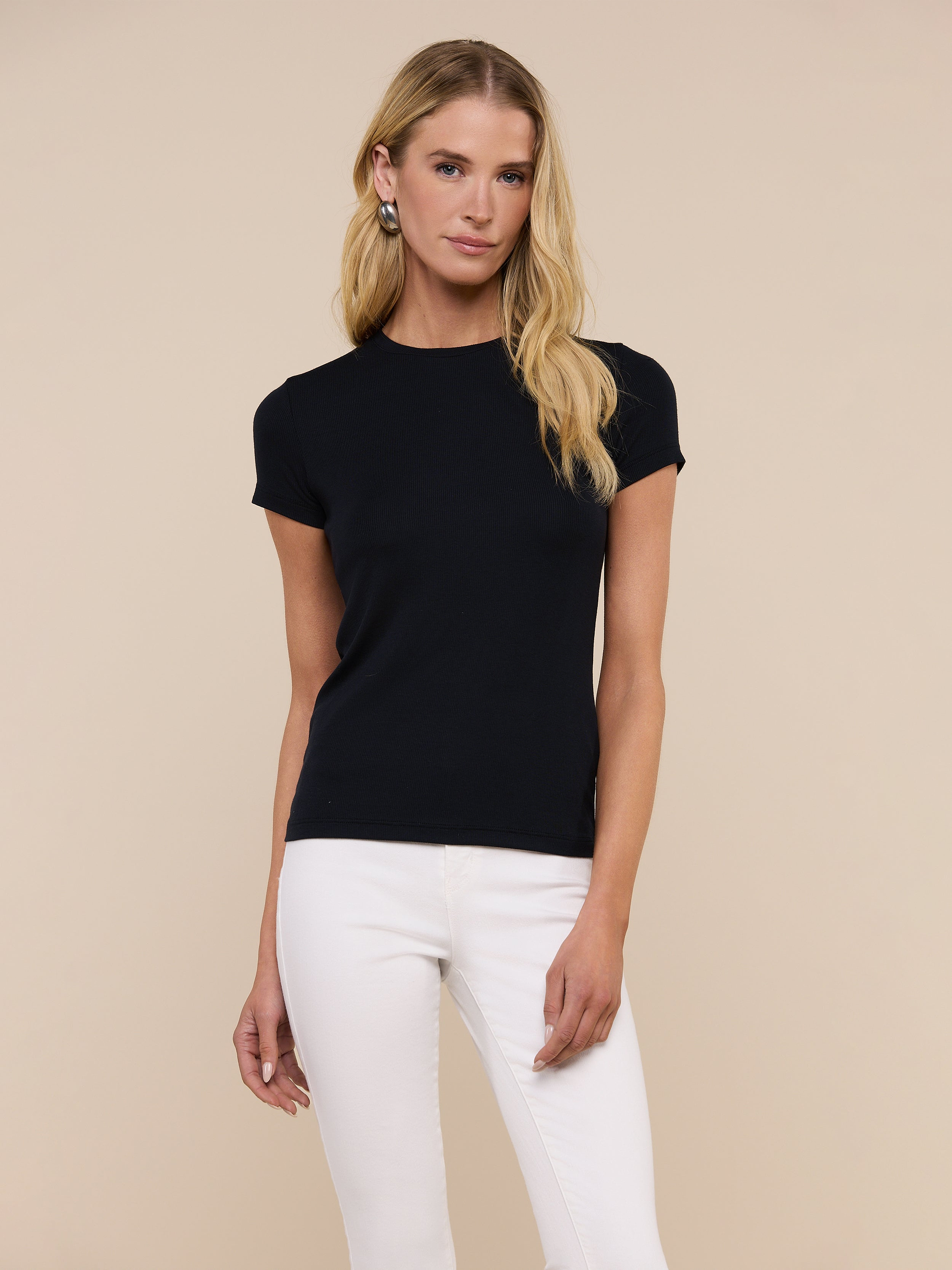 A person with long blonde hair wears the slim-fit, short-sleeve black Ressi Micro-Rib Tee and white pants, standing against a plain light background.