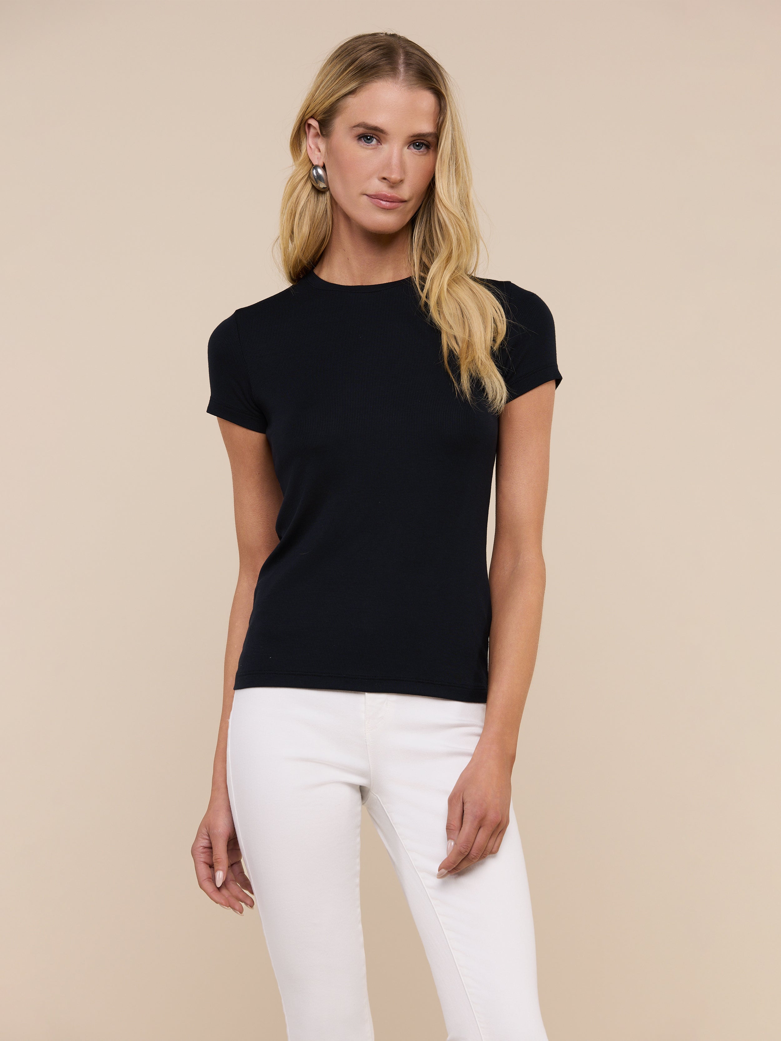 A person with long blonde hair wears the slim-fit, short-sleeve black Ressi Micro-Rib Tee and white pants, standing against a plain light background.