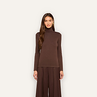A woman stands against a plain background wearing the Lani Turtleneck in dark java brown with loose brown pants, her hair down and hands at her sides.