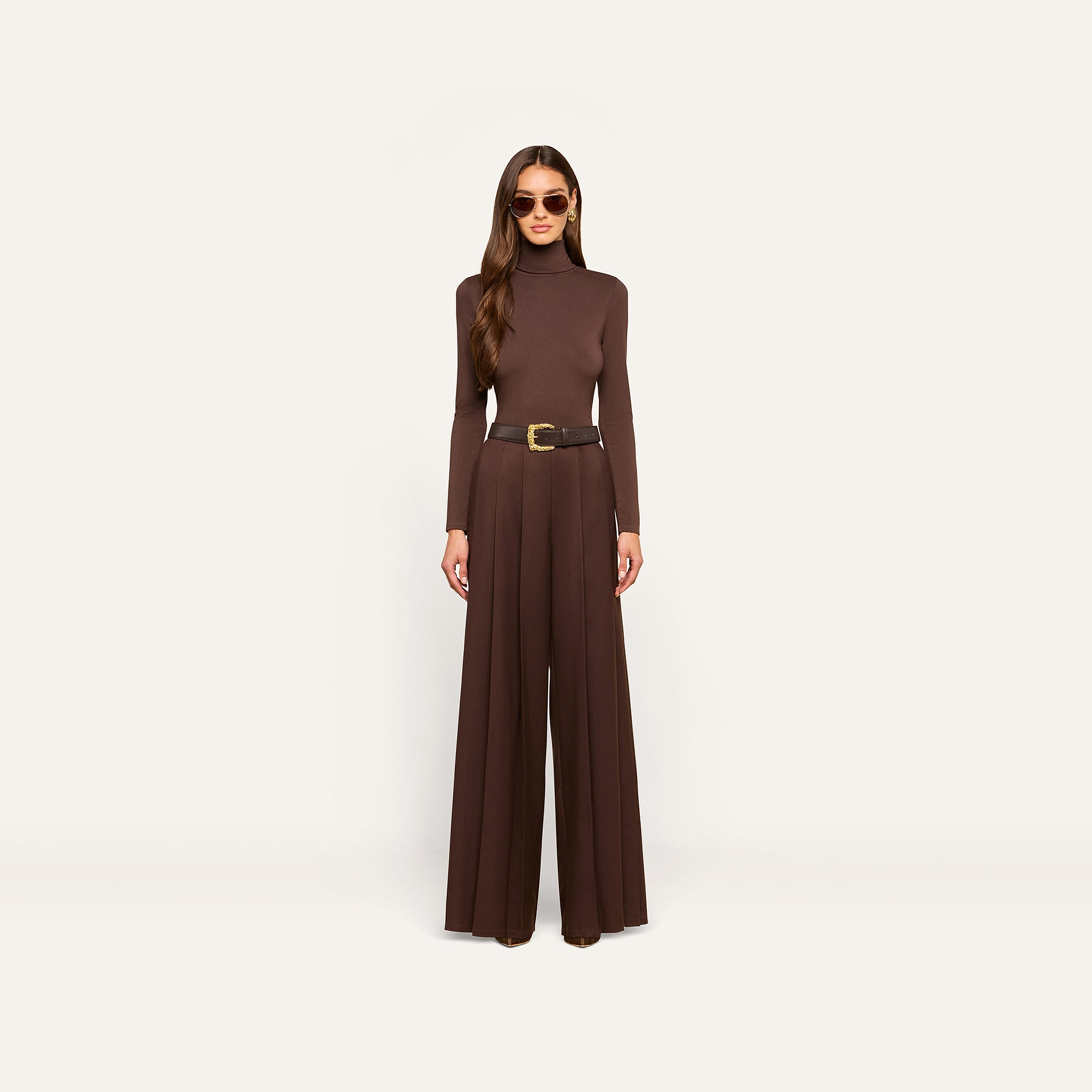 Woman standing against a plain background, wearing the dark java brown Lani Turtleneck in a slim fit, matching wide-leg pants, a black belt with a gold buckle, and sunglasses.