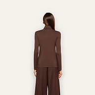 A woman with straight brown hair stands facing away, wearing the slim fit Lani Turtleneck in dark java brown and wide-leg brown pants against a plain, light background.
