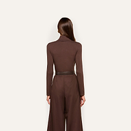 Woman standing with her back to the camera, wearing the Lani Turtleneck in dark java brown, tucked into high-waisted brown wide-leg pants, against a plain light background.