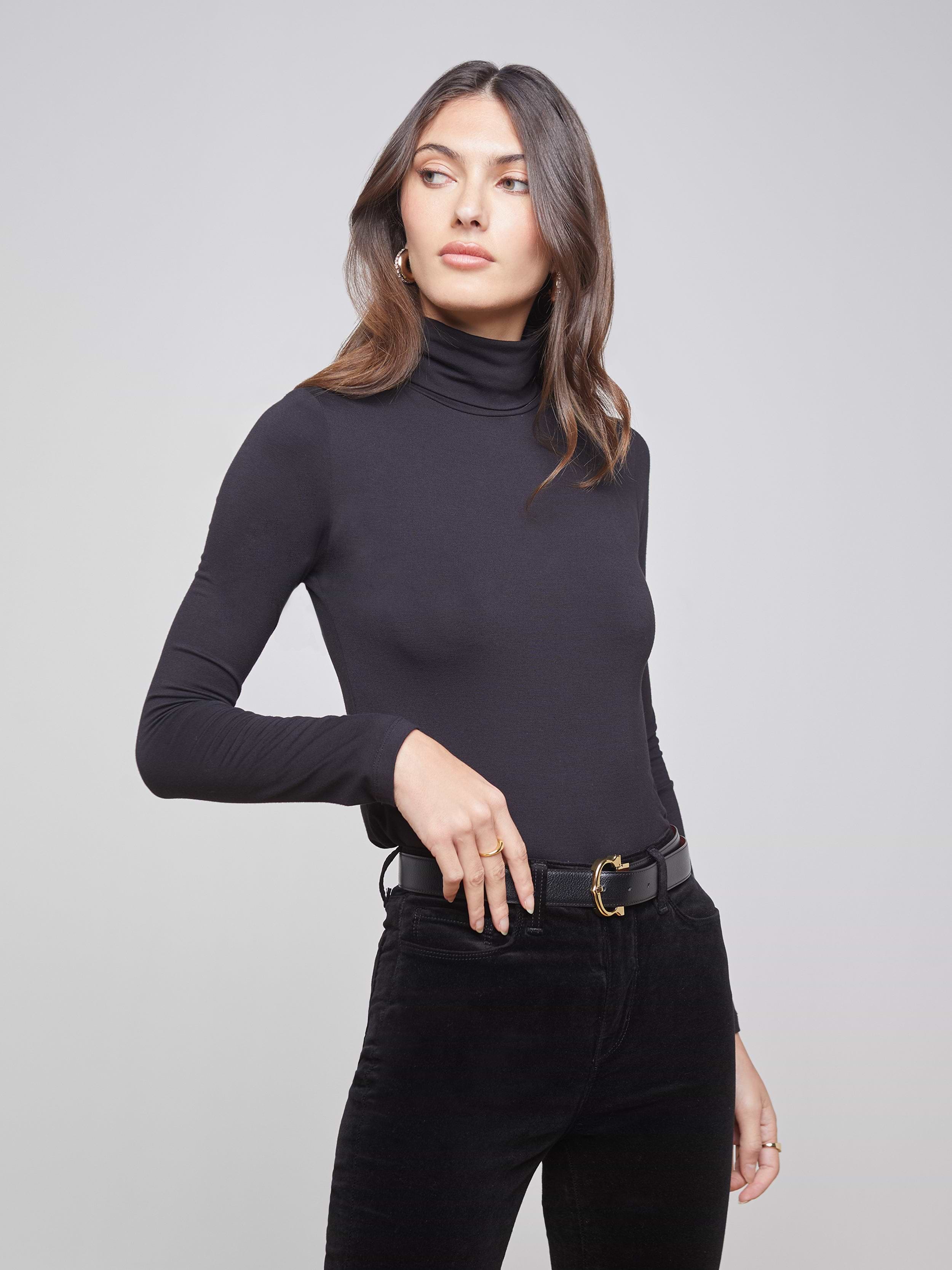Wearing the Lani Turtleneck and black belted pants, a woman stands against a plain light background, looking to the side with one hand on her hip.