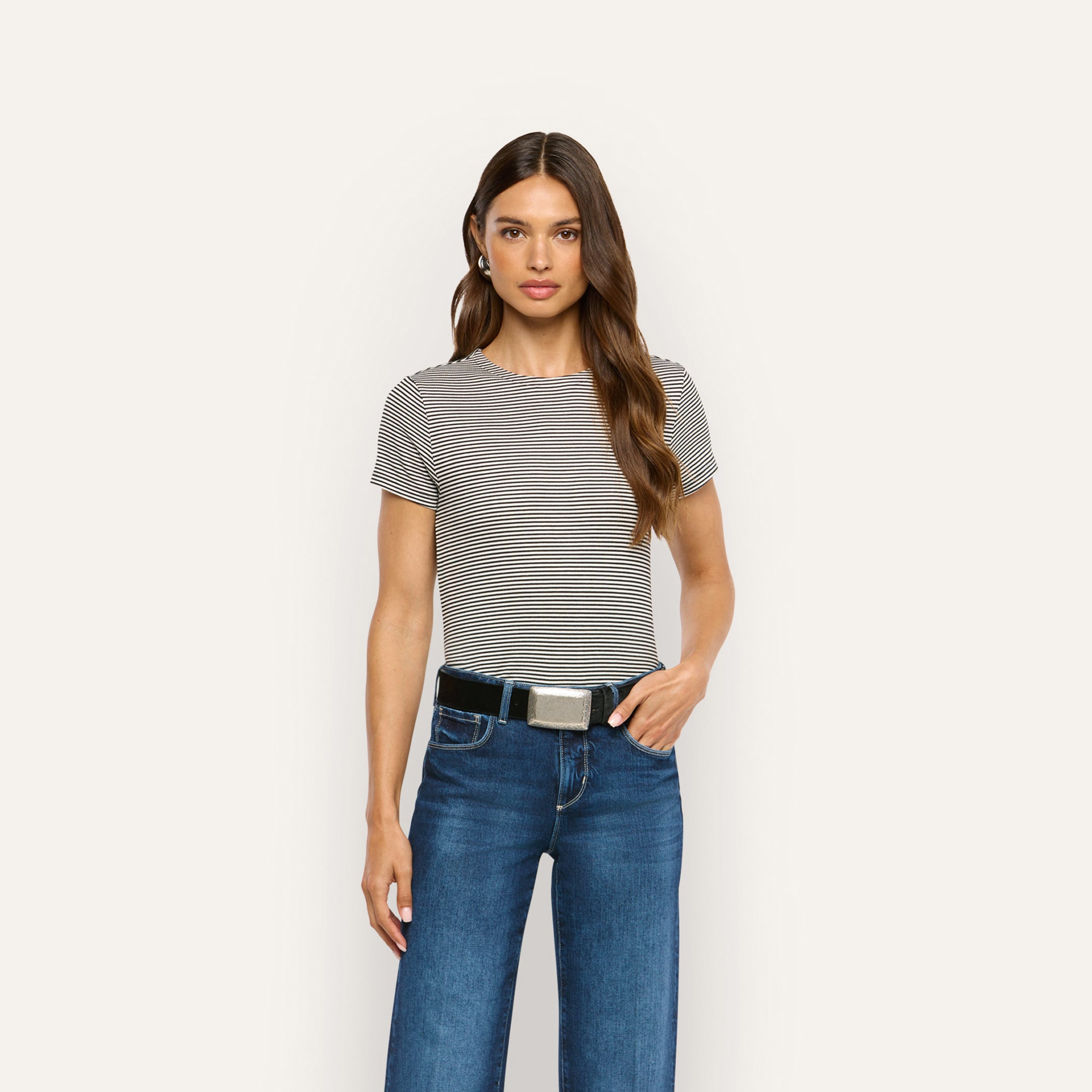 A woman wears a black and white striped ribbed knit Ressi Fitted Tee tucked into blue jeans with a black belt.