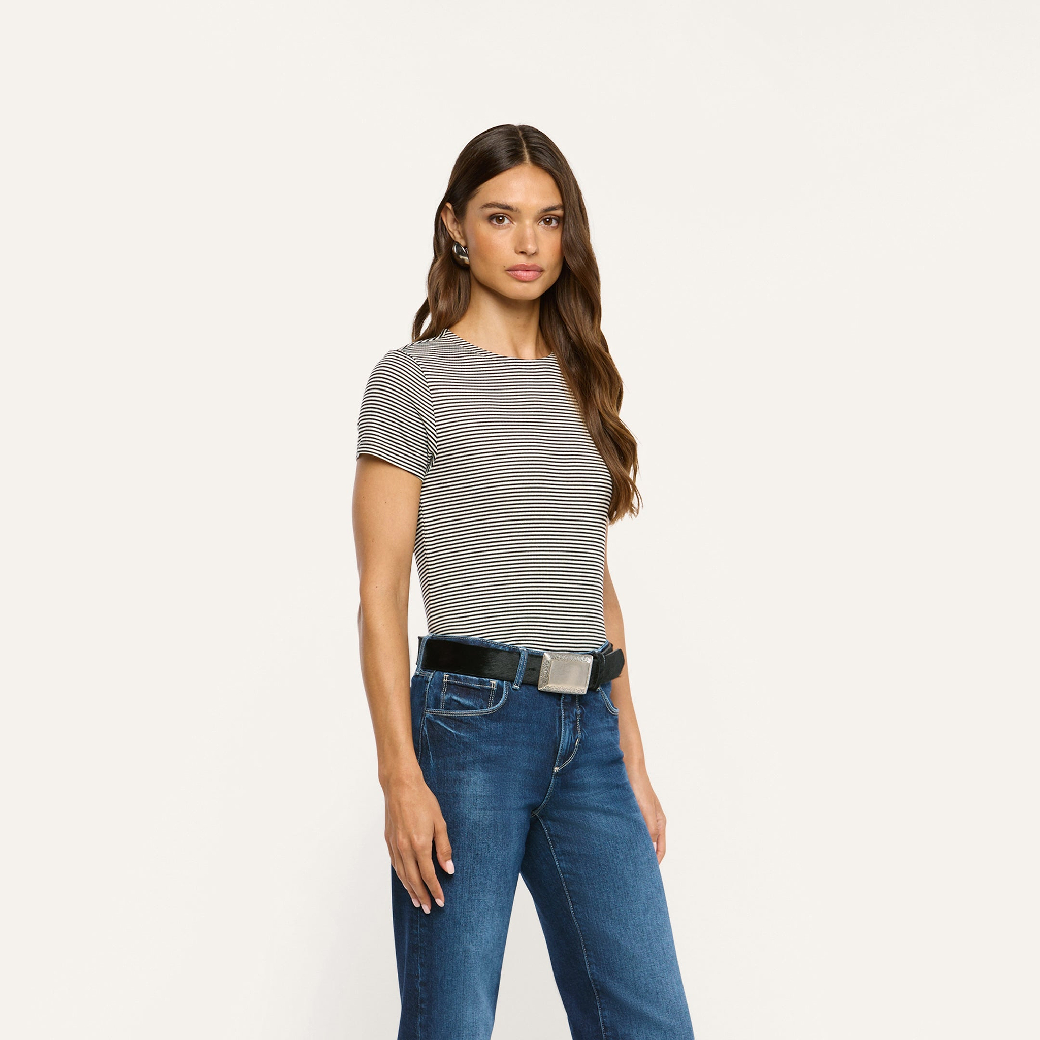 A woman wears a black and white striped ribbed knit Ressi Fitted Tee tucked into dark wash blue jeans with a black belt.