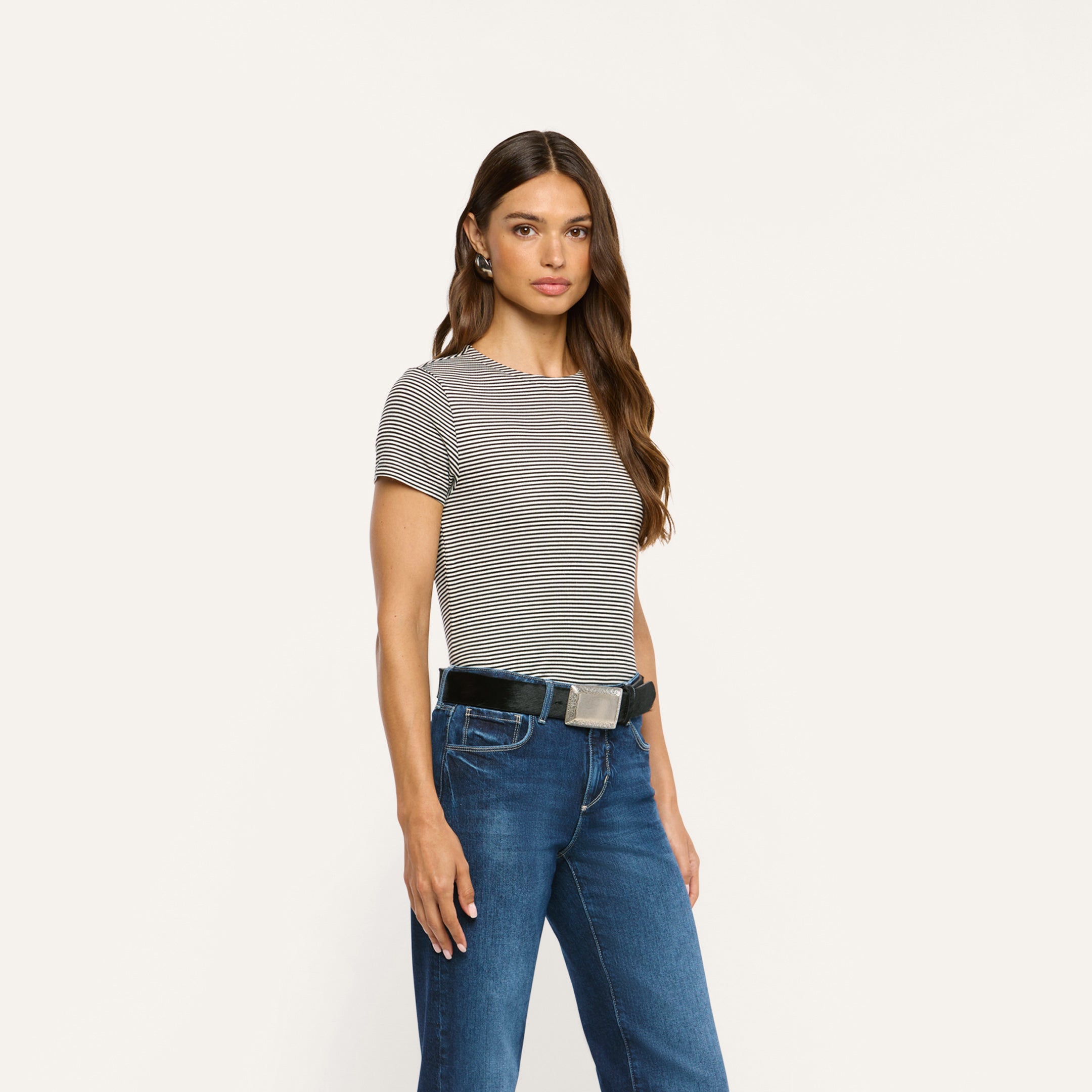 A woman wears a black and white striped ribbed knit Ressi Fitted Tee tucked into dark wash blue jeans with a black belt.