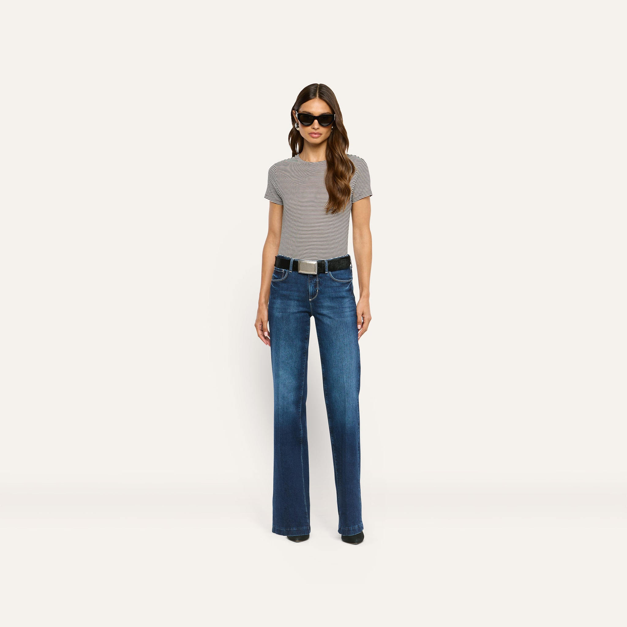 A person wearing a striped ribbed knit Ressi Fitted Tee, dark blue jeans with a black belt, and sunglasses.