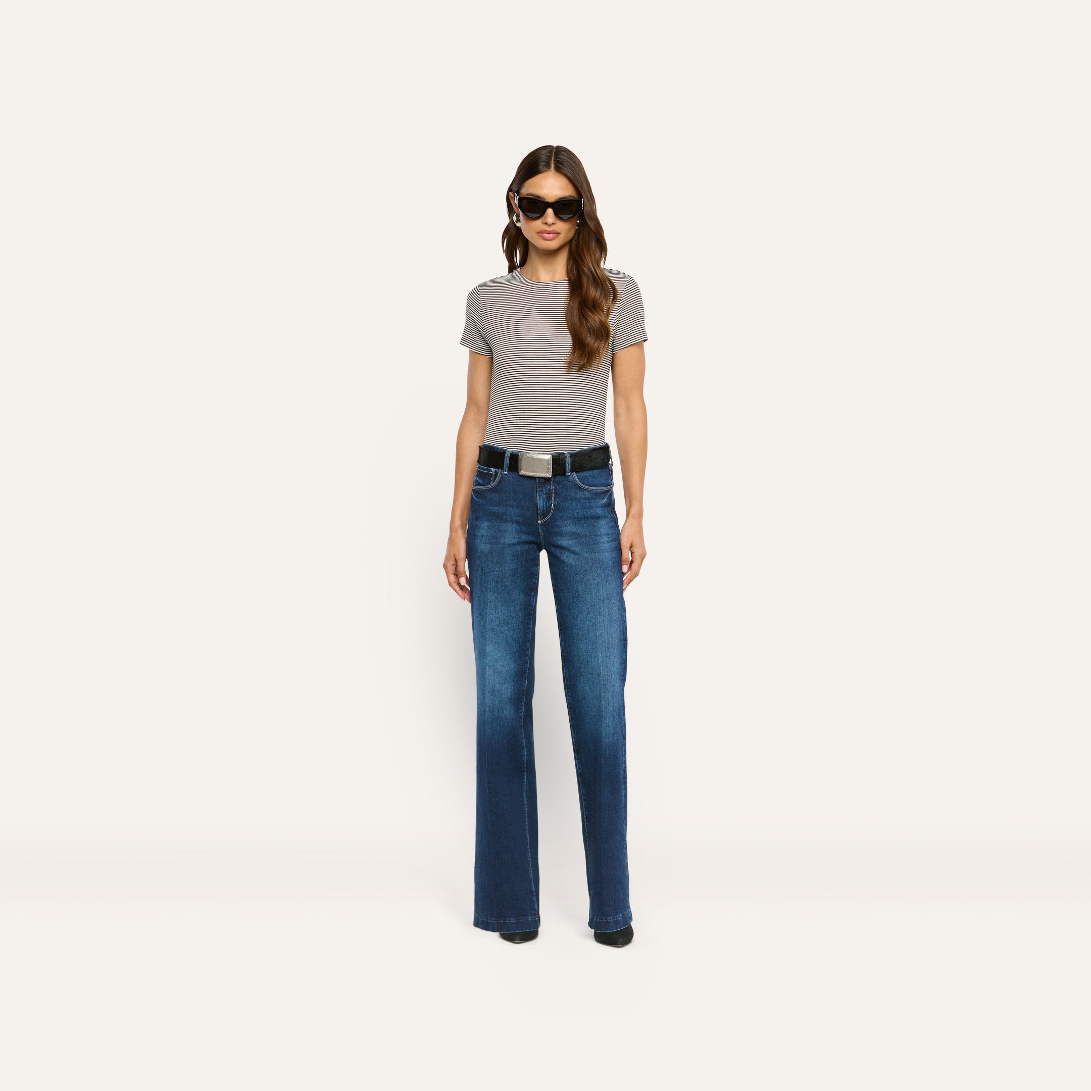 A person wearing a striped ribbed knit Ressi Fitted Tee, dark blue jeans with a black belt, and sunglasses.