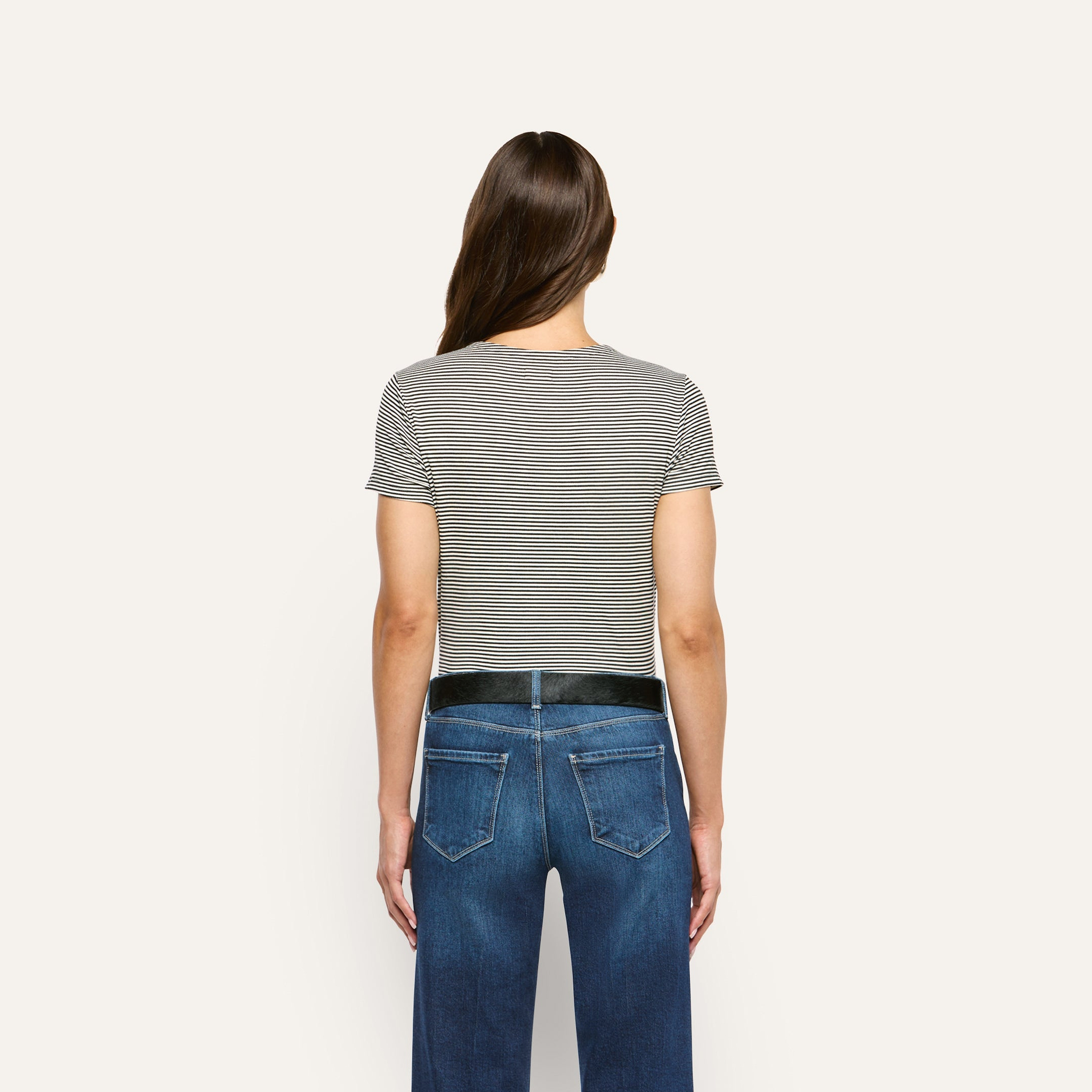 Back view of a person wearing a slim fit, black and white striped Ressi Fitted Tee tucked into blue jeans with a black belt.