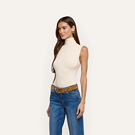 A woman wearing a cream-colored Ceci Sleeveless Turtleneck tucked into blue jeans with a brown suede belt.