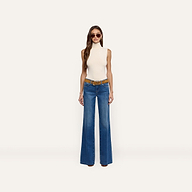 A woman wearing a cream Ceci Sleeveless Turtleneck paired with a brown belt and wide-leg blue jeans.