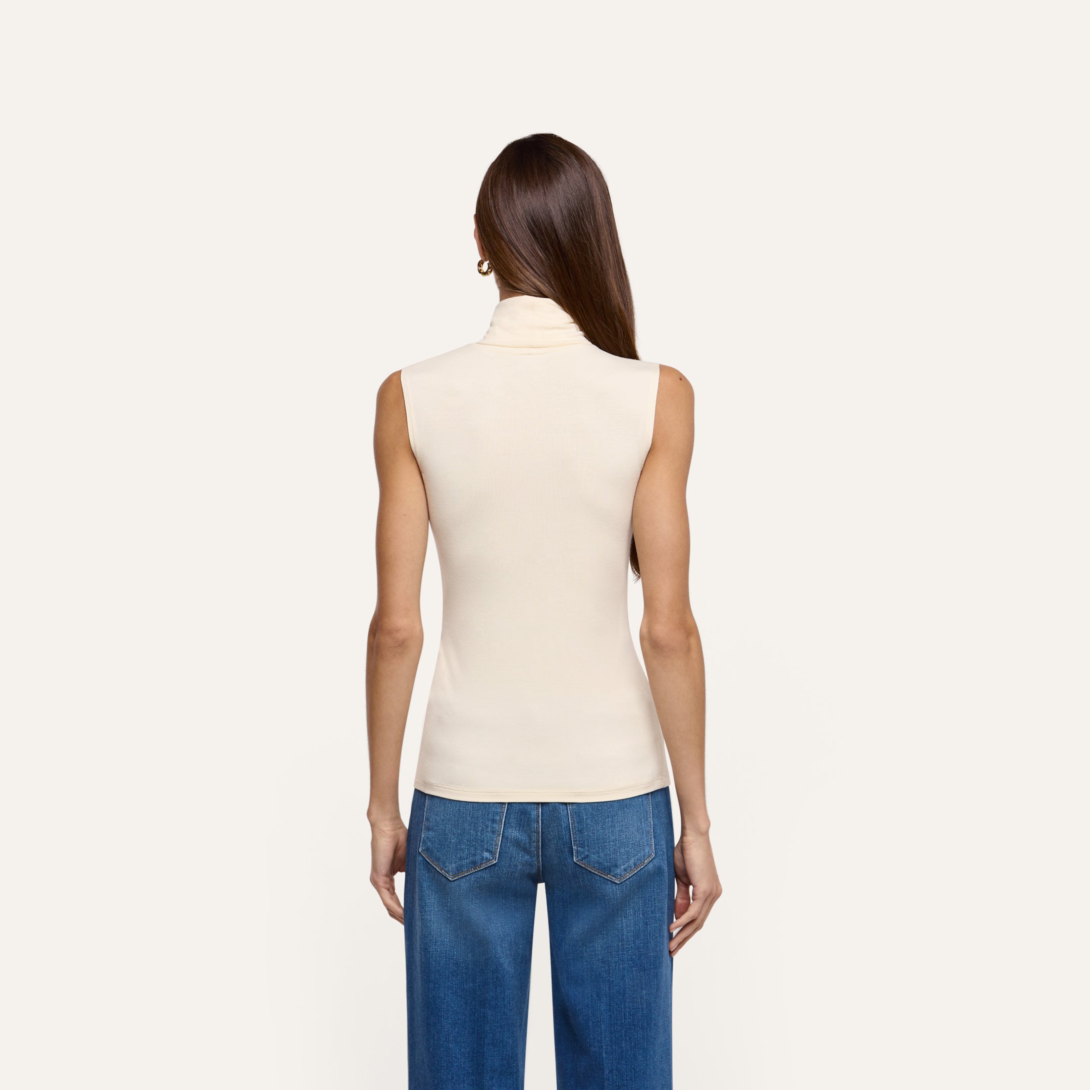 Back view of a person wearing a cream-colored, slim-fit Ceci Sleeveless Turtleneck with blue jeans.