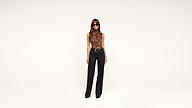 A woman wearing sunglasses, a sleeveless leopard-print top, black belted pants, and black shoes stands against a plain white background.
