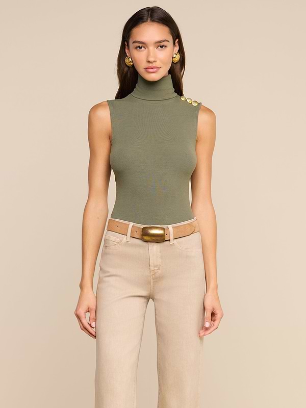 A woman models the Ceci Sleeveless Turtleneck in ash olive green, styled with beige high-waisted pants, a wide brown belt, and gold earrings, standing against a plain light background.