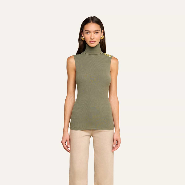 A woman models the Ceci Sleeveless Turtleneck in ash olive green—a ribbed knit top with gold shoulder buttons—paired with beige pants, standing against a plain light background and facing forward.