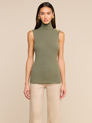 A woman stands facing forward against a plain beige background, wearing the Ceci Sleeveless Turtleneck in ash olive green with gold buttons on the shoulder and paired with beige pants.