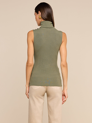 A woman stands facing away, wearing the Ceci Sleeveless Turtleneck in ash olive green ribbed knit paired with beige pants. She has straight brown hair and gold earrings, set against a plain beige background.