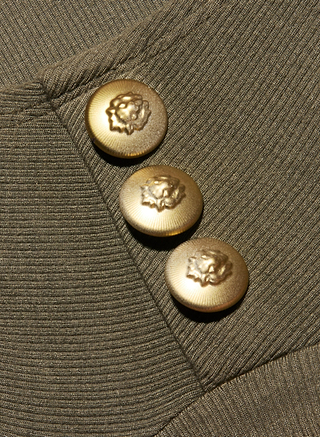 Three gold buttons embossed with lion head designs are sewn in a diagonal row onto the ash olive green ribbed knit fabric of the Ceci Sleeveless Turtleneck.