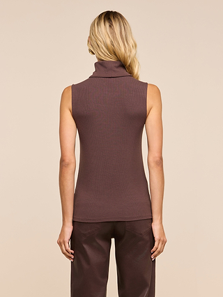 A woman with long blonde hair is shown from the back, wearing a slim-fit, sleeveless brown Ceci Sleeveless Turtleneck crafted from stretch rib knit, paired with dark brown pants, standing against a plain beige background.