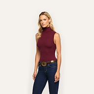 A woman wears a slim-fit, sleeveless burgundy Ceci Sleeveless Turtleneck in a stretch rib knit tucked into dark blue jeans with a decorative western-style belt.