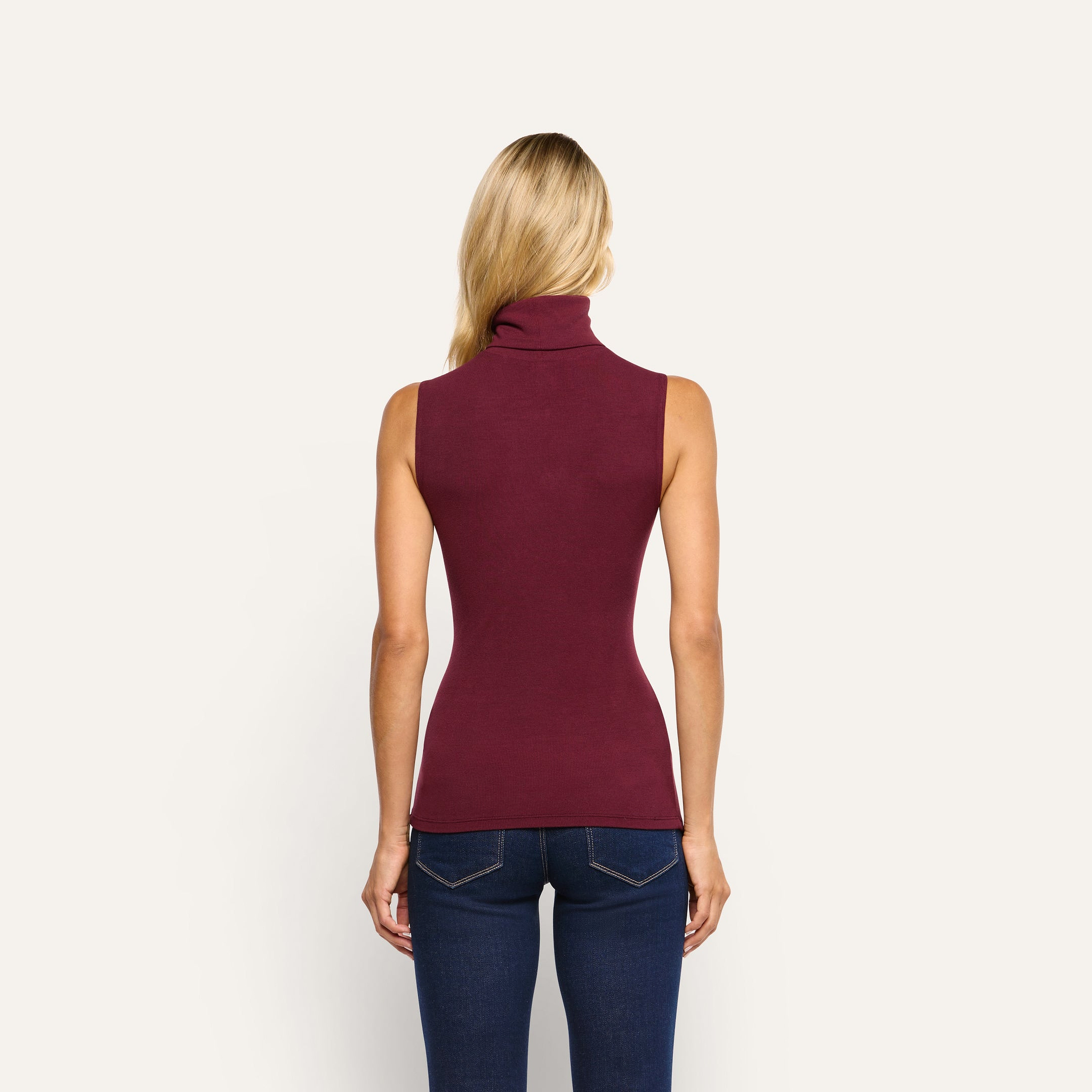 Back view of a person wearing a slim-fit, burgundy stretch rib knit Ceci Sleeveless Turtleneck and dark blue jeans.