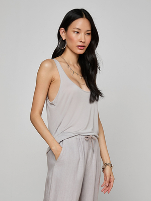 A woman with long black hair wears the Celia Scoopneck Tank and matching drawstring pants, accessorized with hoop earrings, layered necklaces, and a bracelet, standing against a plain light background.