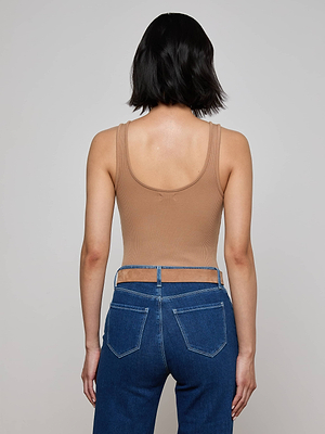 A person with short dark hair faces away from the camera, wearing a tan L'AGENCE Nica Scoopneck Bodysuit and high-waisted blue jeans with cutout waistband details. The background is plain and light-colored.