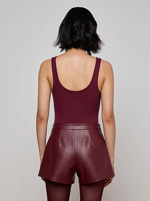 A person with short dark hair is seen from behind against a plain light background, wearing the Nica Scoopneck Bodysuit and high-waisted maroon leather shorts.