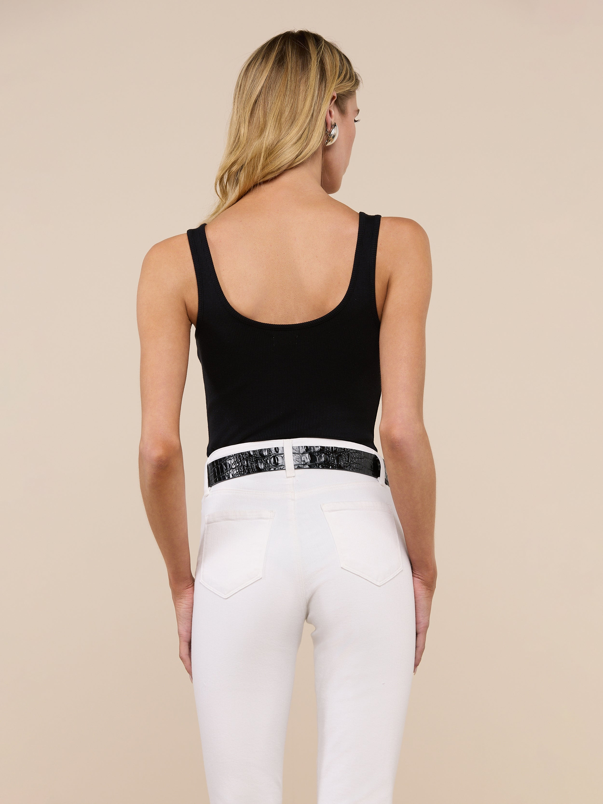 A woman with long blonde hair is shown from the back against a plain light background, wearing the Nica Scoopneck Bodysuit in black, paired with blue jeans and a brown belt.
