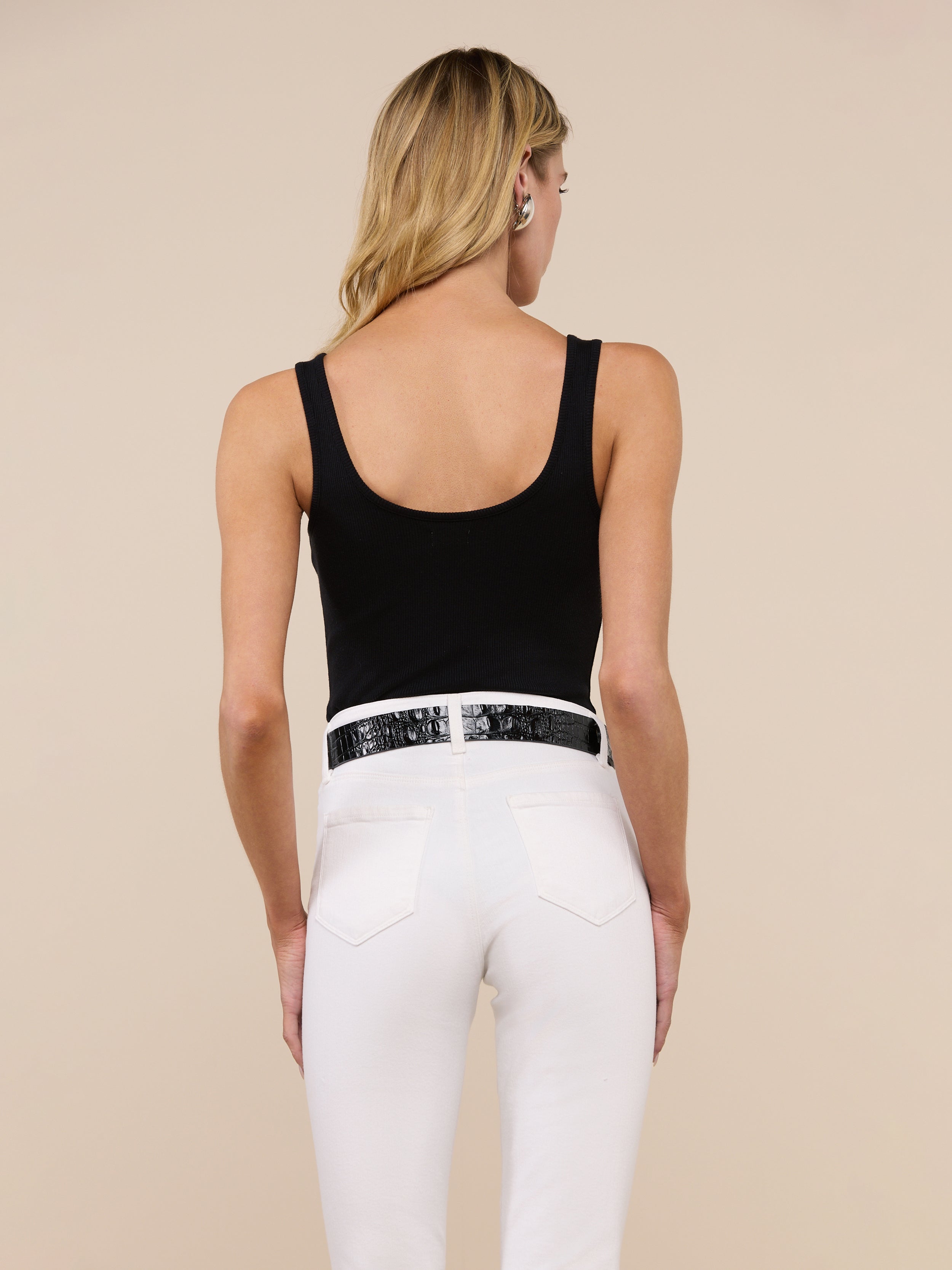 A woman with long blonde hair is shown from the back against a plain light background, wearing the Nica Scoopneck Bodysuit in black, paired with blue jeans and a brown belt.