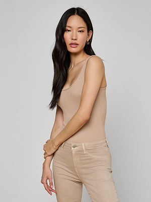 A woman with long black hair wears the Nica Scoopneck Bodysuit in beige and light beige pants, standing against a plain light gray background with her arms gently crossed.