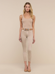 A woman with long dark hair wears the Nica Scoopneck Bodysuit, paired with light beige skinny jeans and nude heels, as she walks indoors on a light wood floor against a plain white wall.